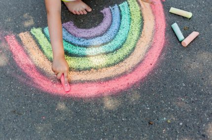 the child girl draws a rainbow with colored chalk on the asphalt.