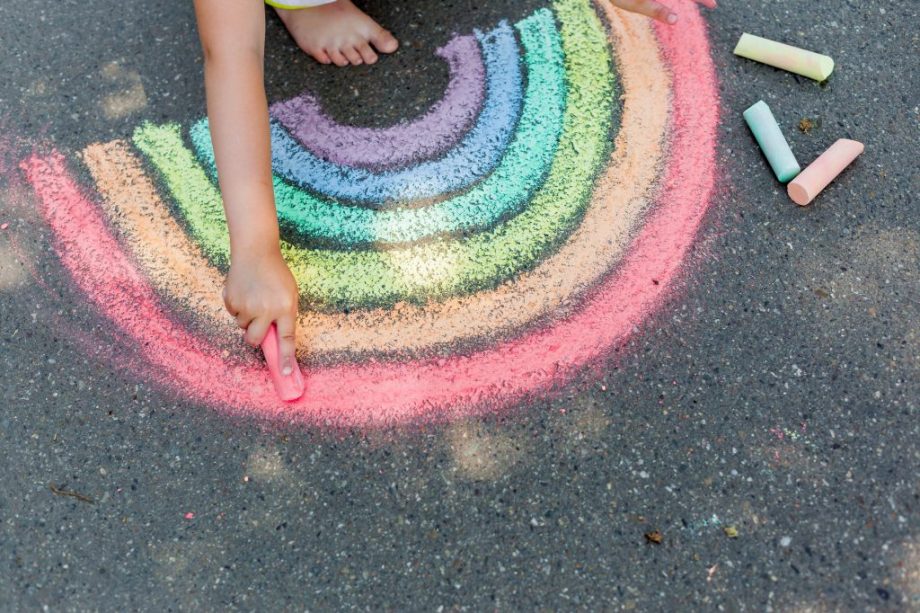 the child girl draws a rainbow with colored chalk on the asphalt.
