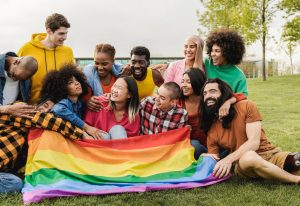 Happy diverse friends holding LGBT rainbow flag having fun together outdoors.
