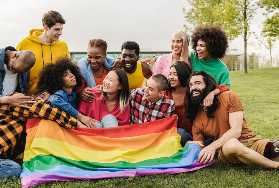 Happy diverse friends holding LGBT rainbow flag having fun together outdoors.